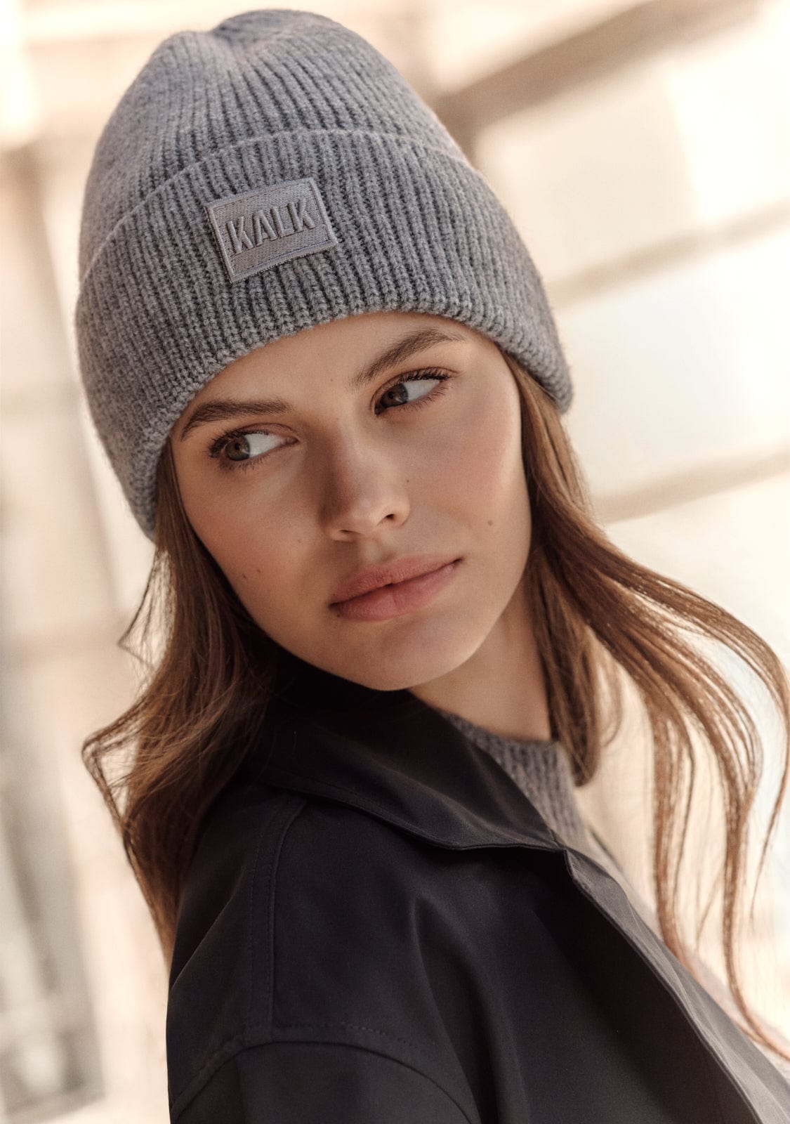 Woman wearing a gray knit beanie with a brand logo against a neutral background